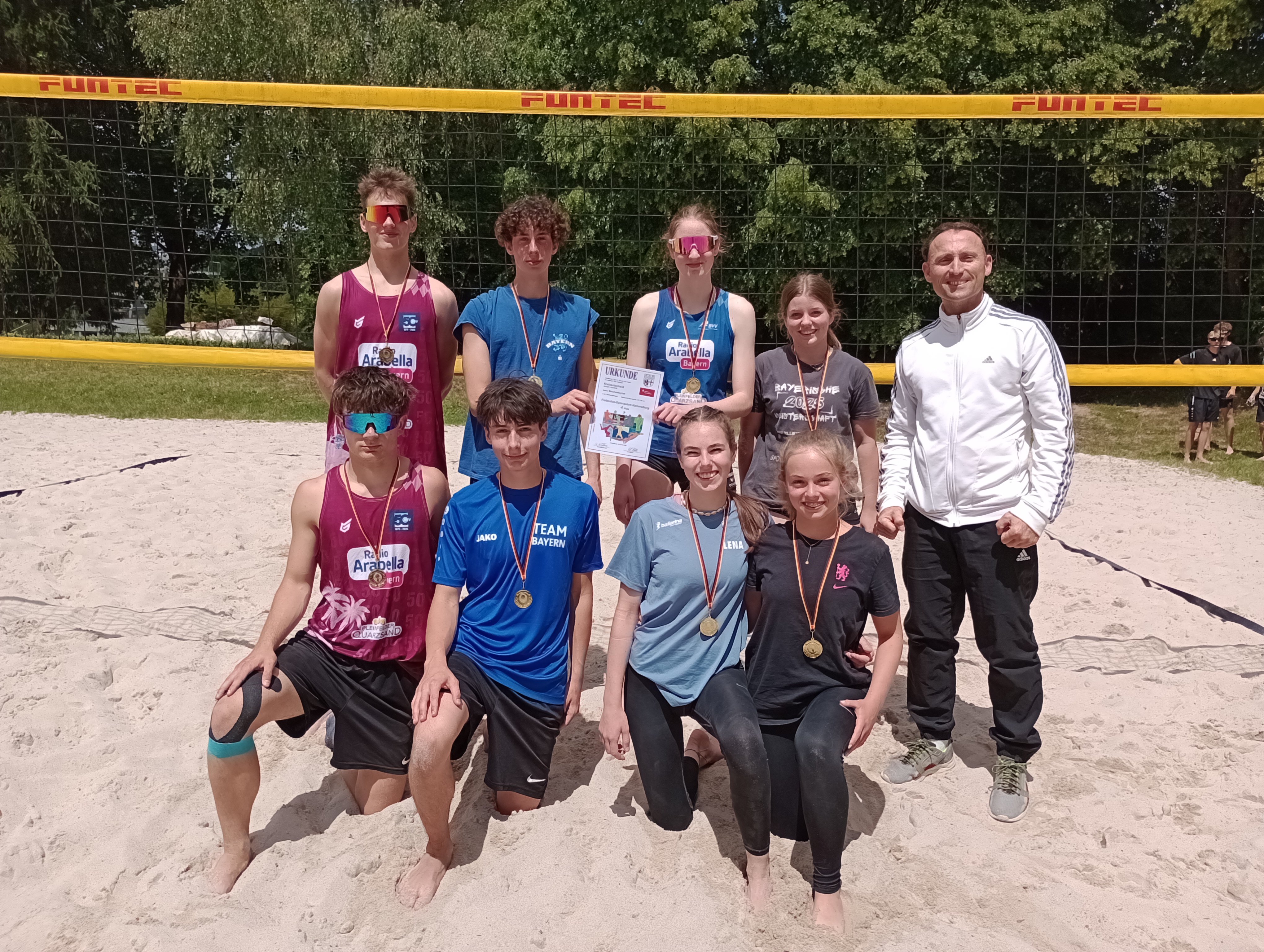 Das Beachvolleyball-Team des Frobenius-Gymnasiums mit Medaillen und Urkunde vor dem Netz im Hammelburger Schwimmbad
