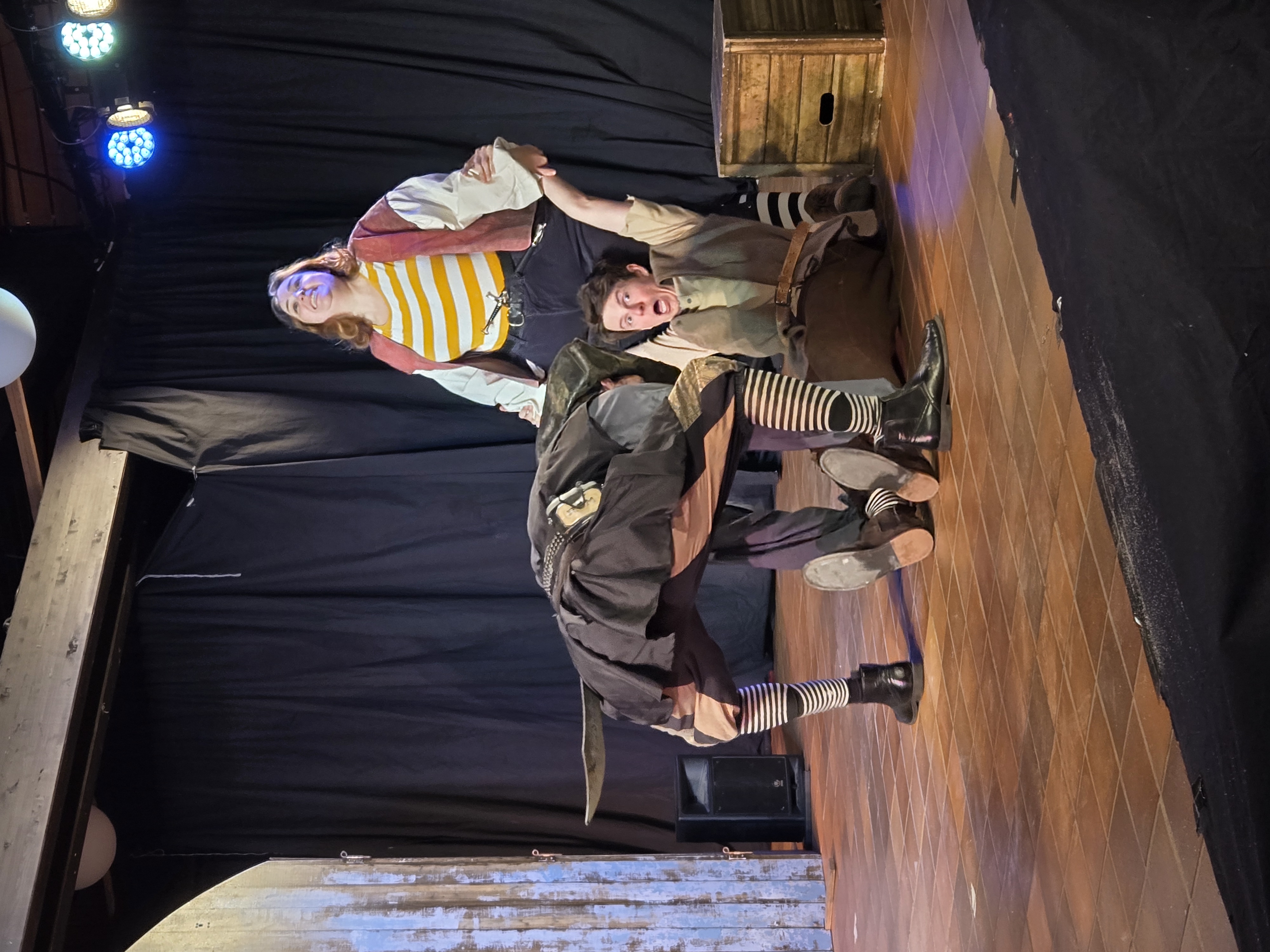 Darstellerinnen und Darsteller in Piratenkostümen spielen eine humorvolle Szene aus „The Tiger of the Seas“ auf der Bühne.