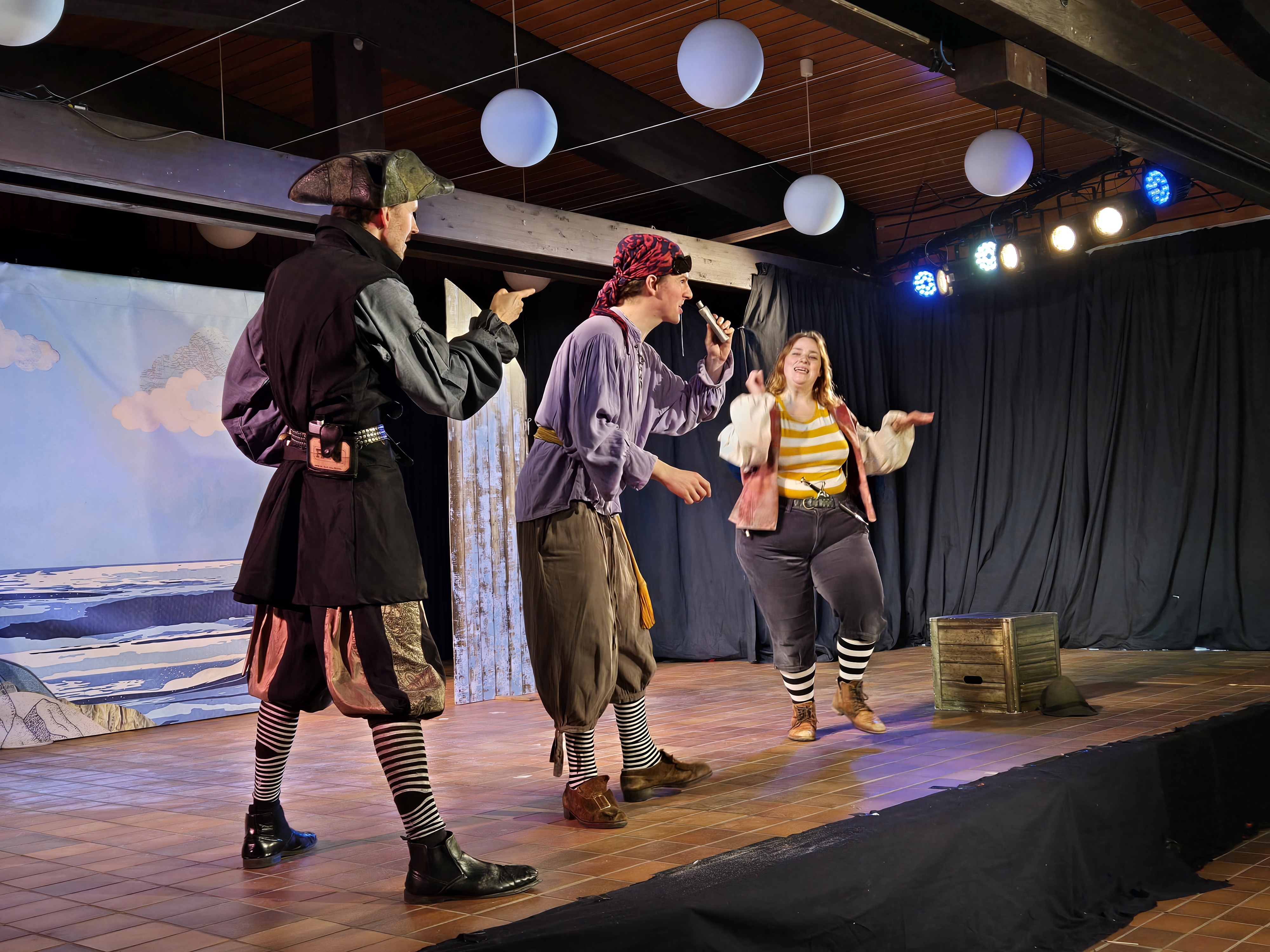 Drei Darstellerinnen und Darsteller des White Horse Theatre spielen eine lebhafte Szene auf der FGH-Bühne.